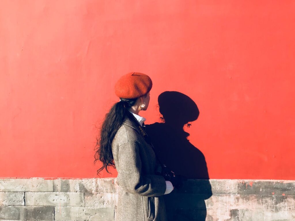 A person standing in profile against an orange wall, looking at their shadow in soft afternoon light.